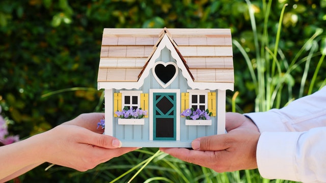 Two people holding a miniature wooden house.
